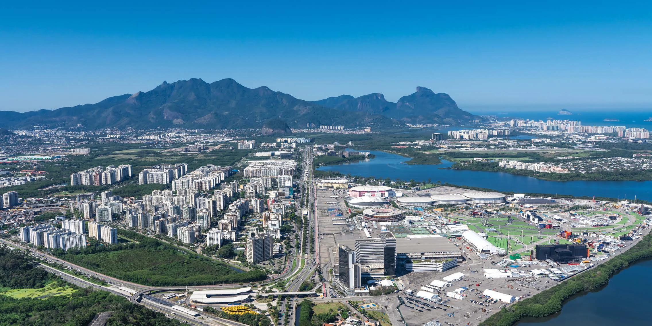 Fotografia aérea da Barra Olímpica, com o Parque Olímpico, a lagoa e as montanhas ao fundo